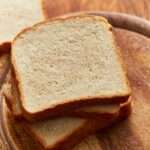 A golden loaf of homemade gluten free bread, sliced on a wooden board, showing a soft, even crumb and crisp crust.