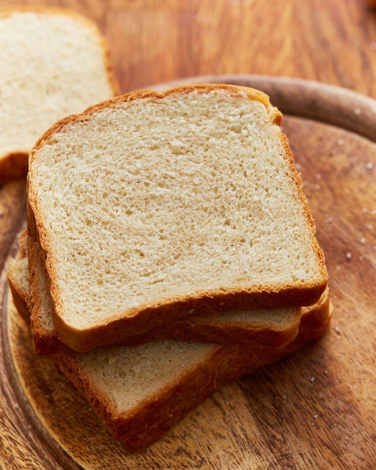 A golden loaf of homemade gluten free bread, sliced on a wooden board, showing a soft, even crumb and crisp crust.