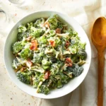 A bowl of loaded broccoli salad with cheddar, bacon, scallions, and creamy dressing, ready to serve.