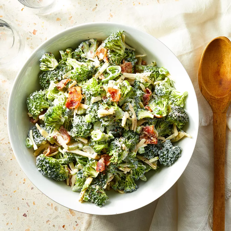 A bowl of loaded broccoli salad with cheddar, bacon, scallions, and creamy dressing, ready to serve.