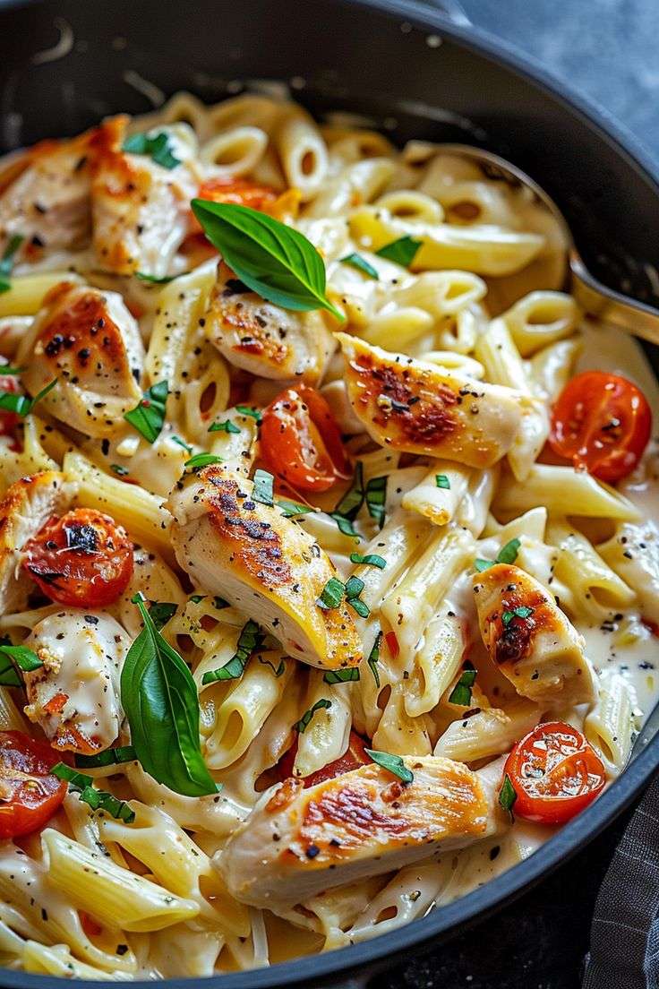 Creamy chicken penne pasta mixed with spinach, cherry tomatoes and Parmesan in a skillet, garnished with fresh basil and parsley.