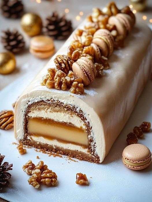 A festive and gourmet vanilla Yule log covered in mascarpone cream, decorated with macarons, nuts and icing sugar, with a swirl of caramel filling visible inside.
