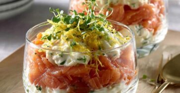 Smoked salmon verrines layered with cream cheese, preserved lemon zest and fresh microgreens served in clear glasses.