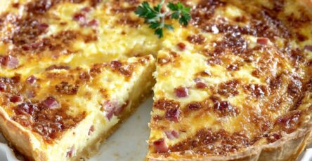 A golden baked classic ham and cheese quiche in a tart tin with a flaky shortcrust pastry, creamy egg custard and melted cheese slices on top.