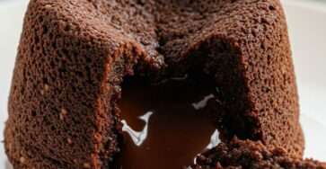 Warm classic chocolate lava cake with molten chocolate center flowing onto plate, dusted with powdered sugar and served with vanilla ice cream.