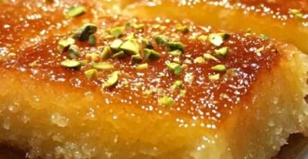 Golden Middle Eastern basbousa cake topped with pistachios and almonds, soaked in syrup and sliced into diamond shapes on a serving tray.