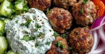 Greek meatball bowl with rice, tzatziki sauce, cherry tomatoes, cucumber slices, red onion and feta cheese served in a ceramic bowl.