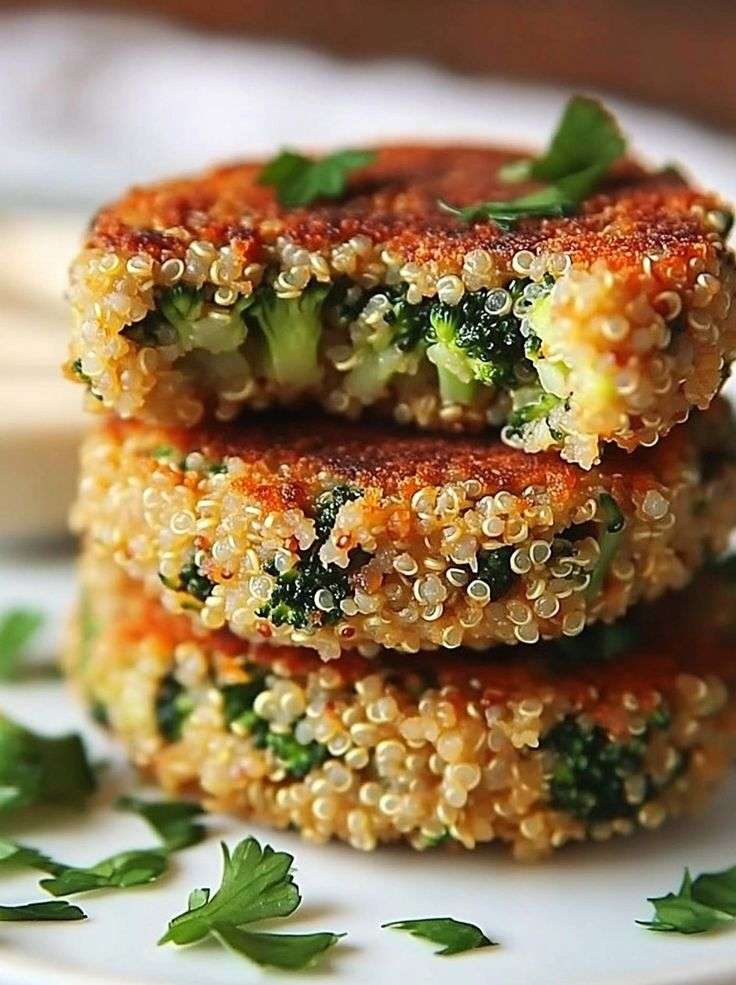 Golden crispy and cheesy broccoli and quinoa patties made with cheese and breadcrumbs, served warm on a plate with dipping sauce.