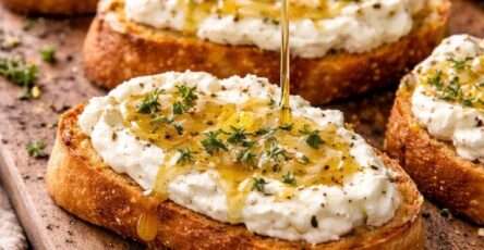 Golden toasted baguette slices topped with whipped feta cheese, drizzled with honey and garnished with fresh thyme leaves on a serving platter. feta and honey crostini