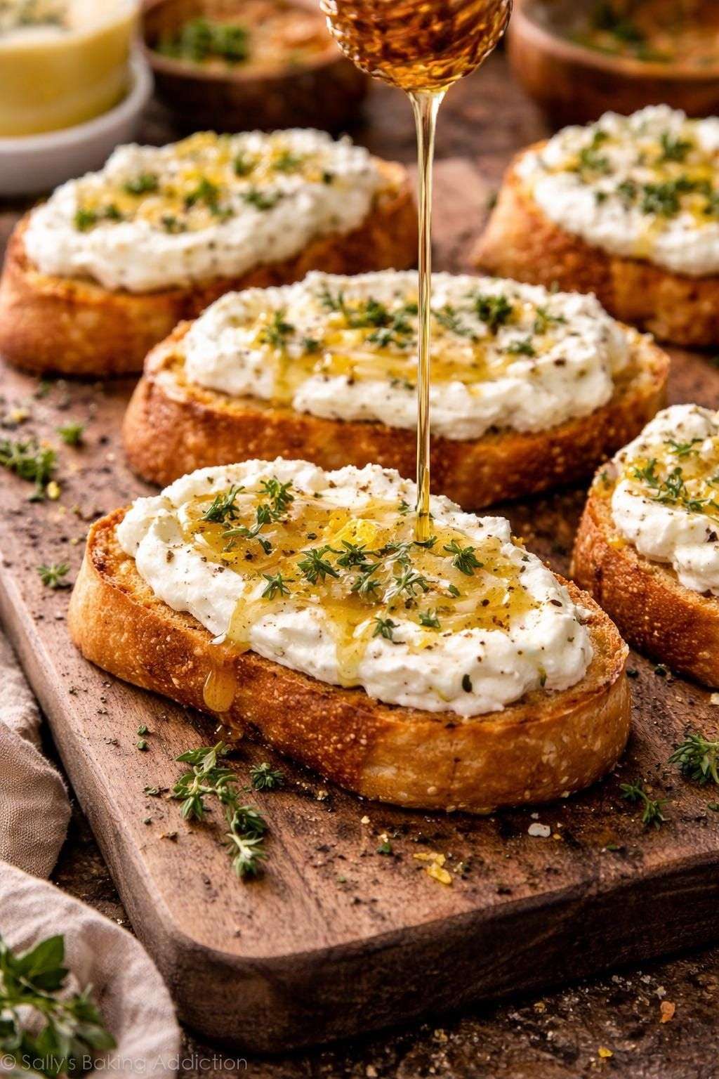Golden toasted baguette slices topped with whipped feta cheese, drizzled with honey and garnished with fresh thyme leaves on a serving platter. feta and honey crostini