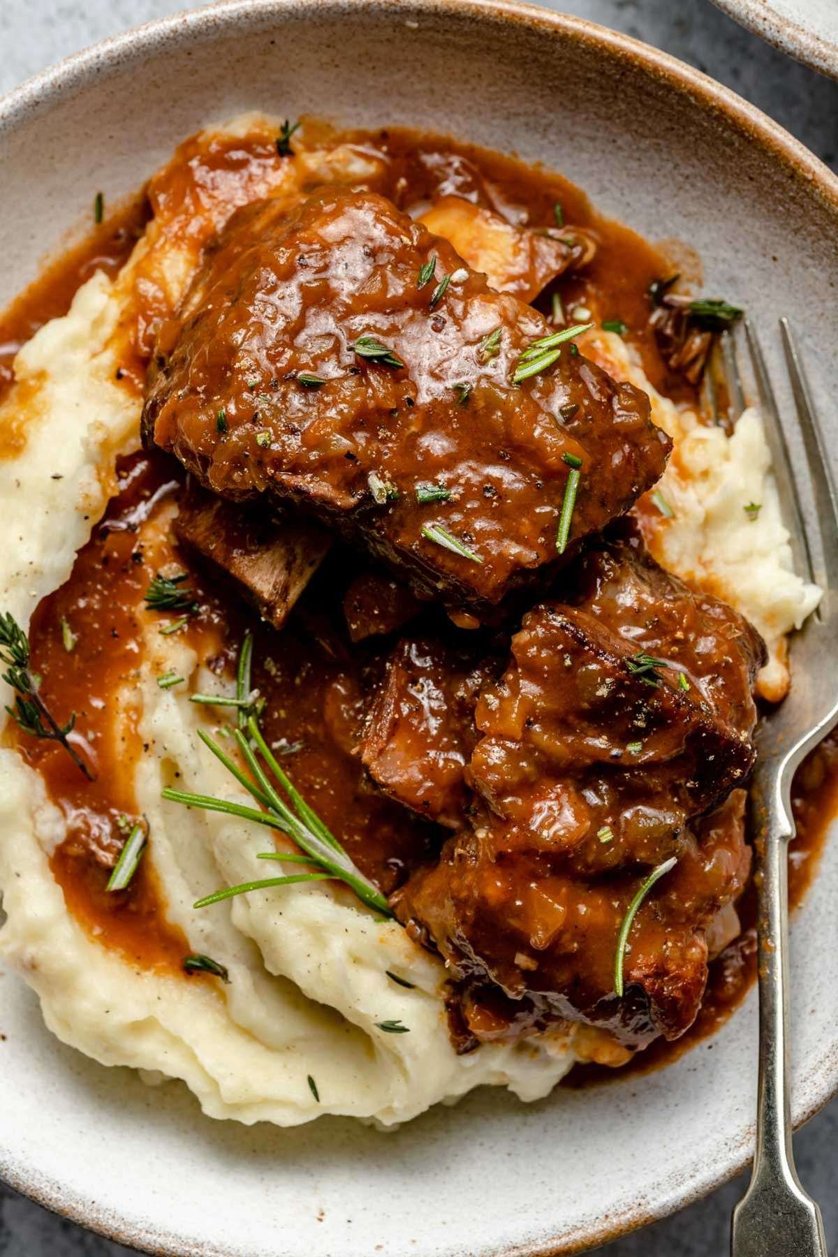 Fork-tender braised beef short ribs simmered in red wine sauce with carrots, onions and herbs, served over creamy mashed potatoes.
