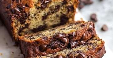 Moist Classic chocolate chip banana bread loaf sliced on a cutting board, showing a soft crumb with melted chocolate chips and ripe banana texture.
