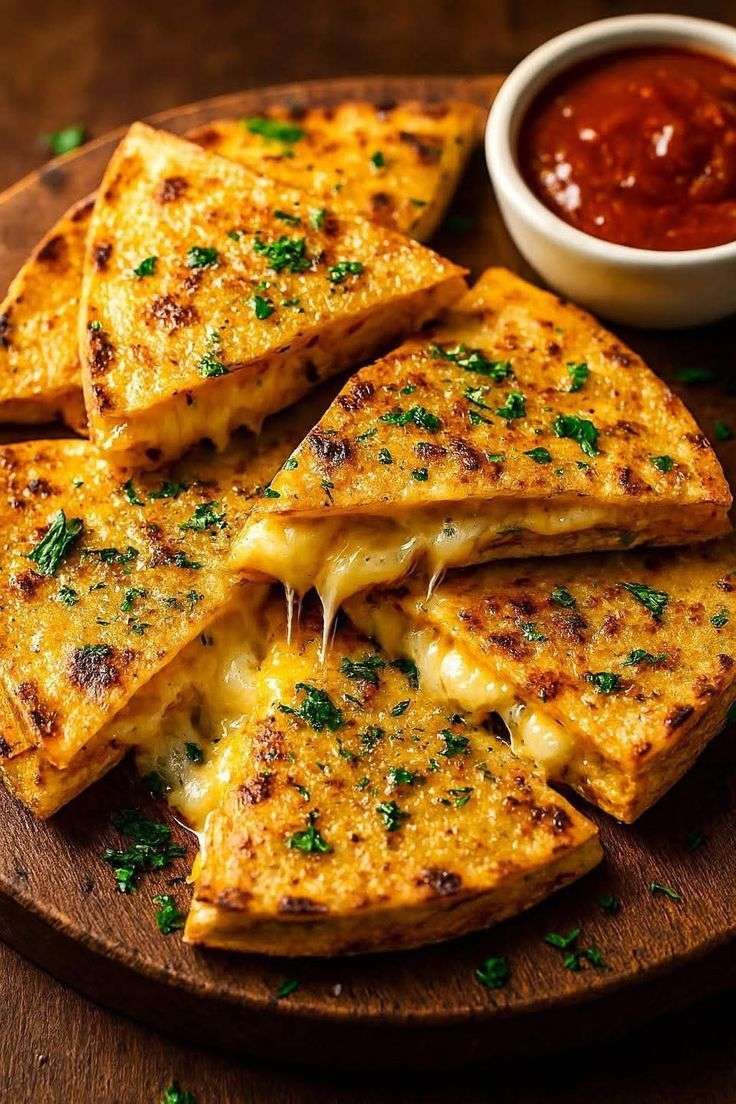 Crispy garlic butter cheese quesadillas sliced into wedges, topped with parsley and served with tomato dipping sauce on a wooden board.