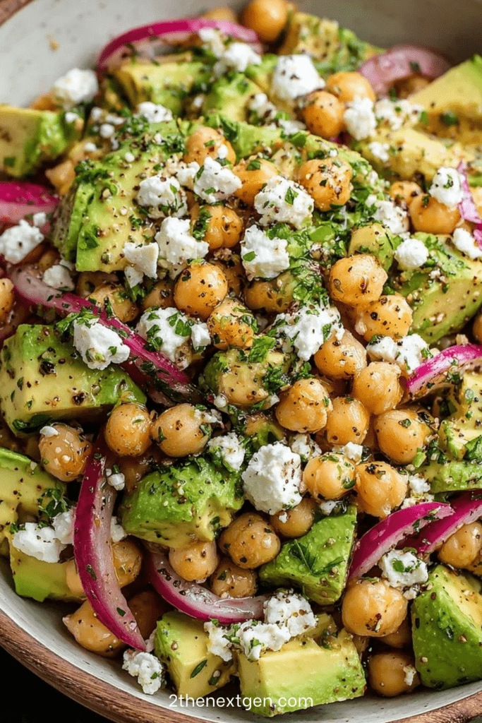 A fresh chickpea avocado feta salad with red onion, parsley and mint tossed in a lemon olive oil dressing and served in a bowl.
