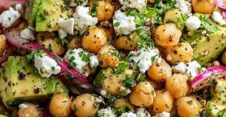 A fresh chickpea avocado feta salad with red onion, parsley and mint tossed in a lemon olive oil dressing and served in a bowl.