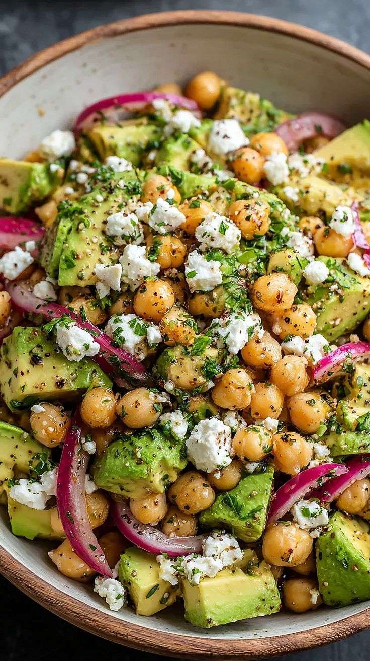 A fresh chickpea avocado feta salad with red onion, parsley and mint tossed in a lemon olive oil dressing and served in a bowl.