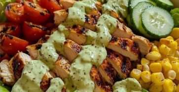 Grilled chicken avocado salad bowl with romaine lettuce, cherry tomatoes, cucumber, corn and creamy avocado dressing served in a ceramic bowl.