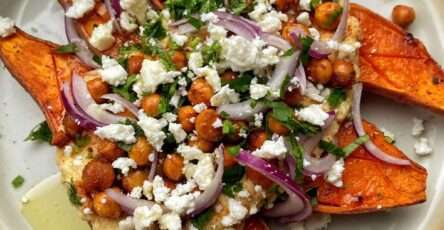 loaded roasted sweet potato halves topped with crispy spiced chickpeas, crumbled feta cheese, red onion and fresh parsley on a baking tray.