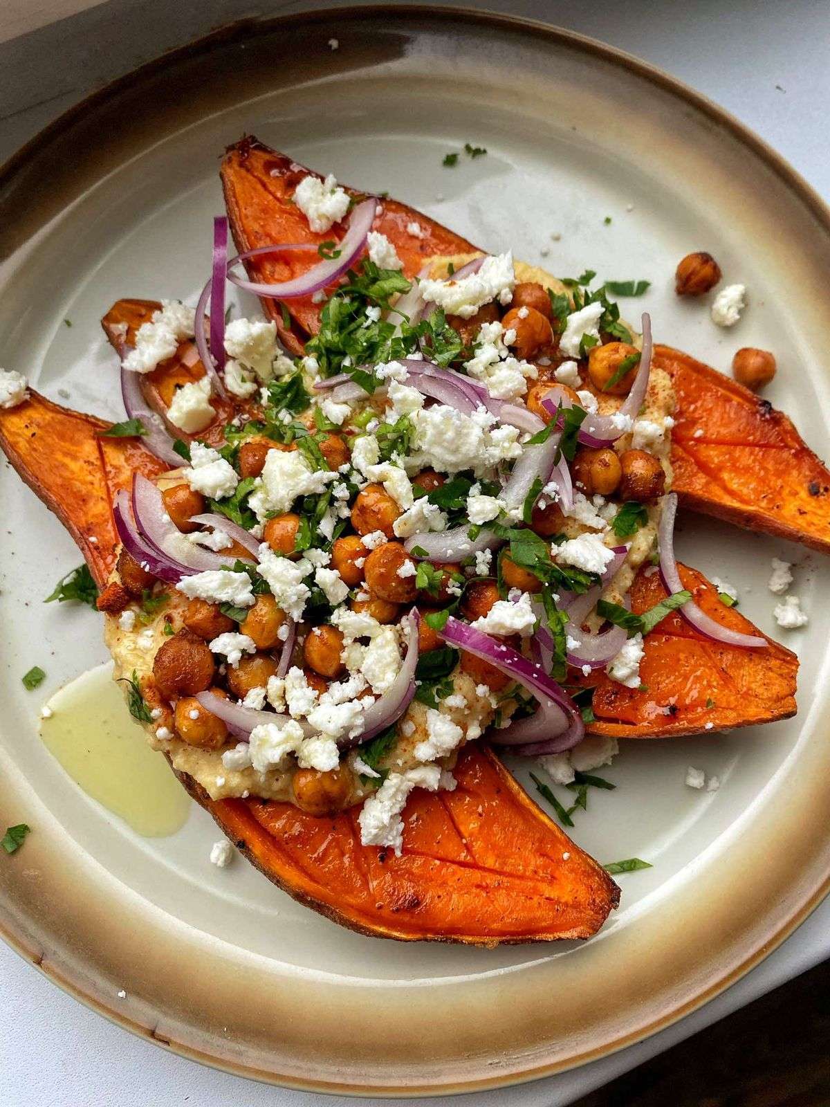 loaded roasted sweet potato halves topped with crispy spiced chickpeas, crumbled feta cheese, red onion and fresh parsley on a baking tray.