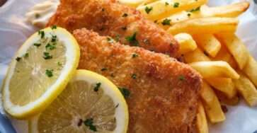 Crispy fish fillets served with golden thick-cut fries and homemade tartar sauce, garnished with lemon wedges on a serving platter.