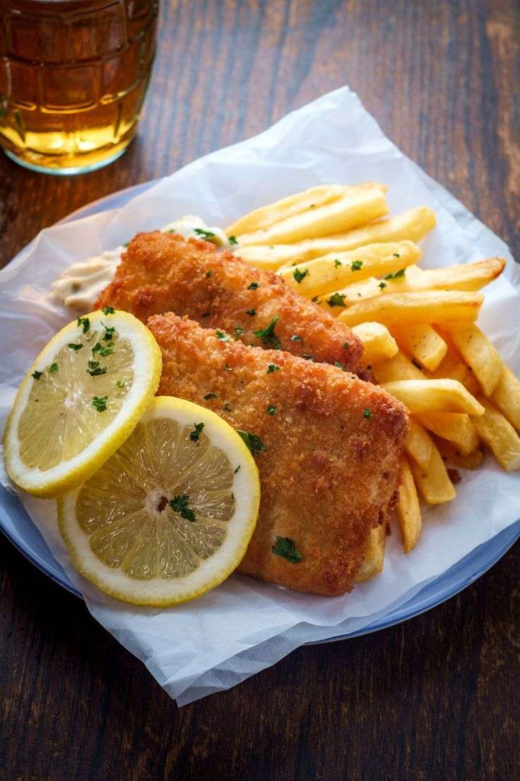 Crispy fish fillets served with golden thick-cut fries and homemade tartar sauce, garnished with lemon wedges on a serving platter.