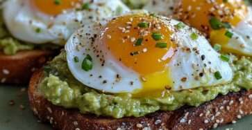 Avocado toast topped with soft-boiled eggs, runny yolk, chives and sesame seeds on whole wheat bread