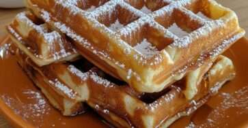 Golden homemade waffles with a crispy exterior and soft center, served with powdered sugar and maple syrup