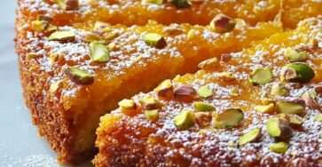 Golden pistachio semolina syrup cake topped with chopped pistachios and powdered sugar, sliced to reveal a moist glossy interior