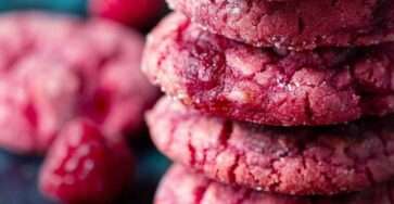 Soft raspberry sugar cookies with vibrant pink color, slightly crinkled tops, chewy centers, and visible raspberry pieces baked to a light golden edge.