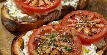 Crispy sourdough toast topped with whipped ricotta cheese, fresh tomato slices, olive oil drizzle, cracked black pepper, and basil leaves. Ricotta and tomato toast.