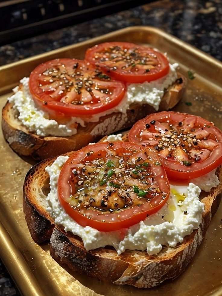 Crispy sourdough toast topped with whipped ricotta cheese, fresh tomato slices, olive oil drizzle, cracked black pepper, and basil leaves. Ricotta and tomato toast.