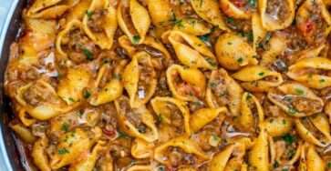 Creamy beef and shells pasta in a skillet with ground beef, tomato cream sauce, melted cheddar cheese, and fresh parsley garnish.