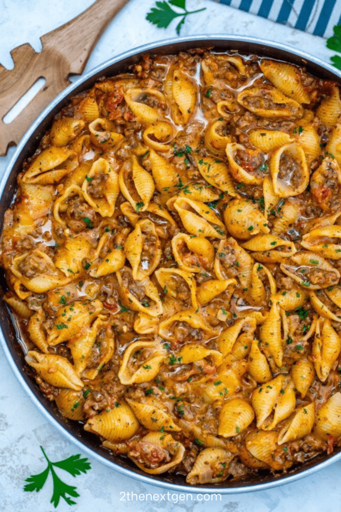 Creamy beef and shells pasta in a skillet with ground beef, tomato cream sauce, melted cheddar cheese, and fresh parsley garnish.