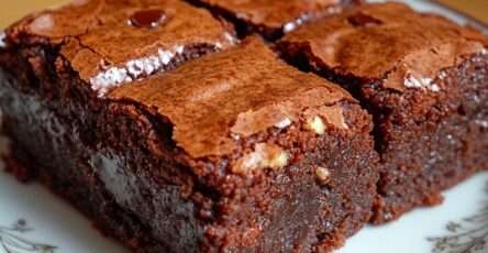 Chocolate brownie with runny center cut into squares, rich dark chocolate texture with gooey molten center flowing from the middle, topped with crushed walnuts on parchment paper
