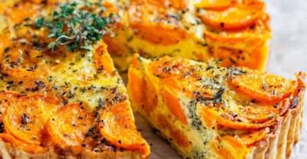 Homemade carrot and herb tart with golden top, sliced carrots and melted cheese baked in a rustic pie dish