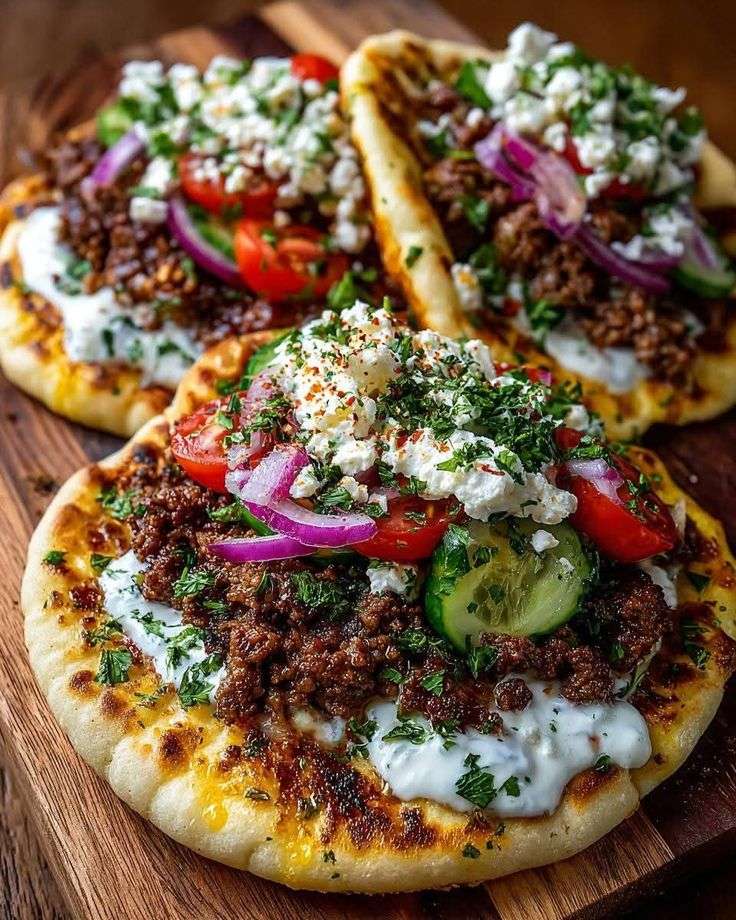 Mini Mediterranean lahmacun bites on crispy flatbread rounds topped with spiced ground beef, cucumber slices, cherry tomatoes, red onion, feta cheese, and garlic yogurt drizzle.