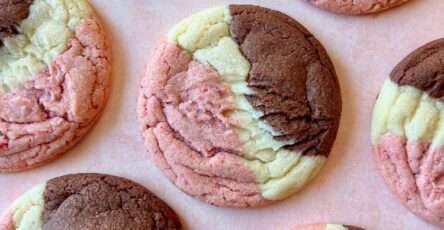 Three-color Neapolitan cookies showing distinct vanilla, strawberry, and chocolate sections baked into one soft, crinkled sugar cookie with a golden edge and vibrant pink center.