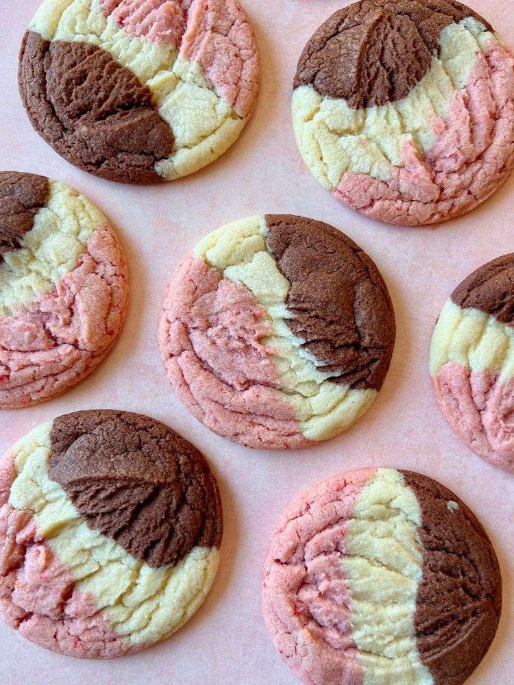 Three-color Neapolitan cookies showing distinct vanilla, strawberry, and chocolate sections baked into one soft, crinkled sugar cookie with a golden edge and vibrant pink center.