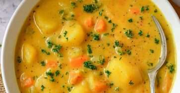 A bowl of classic German Kartoffelsuppe made with potatoes, carrots, leeks, celery, fresh parsley, and sliced sausages, served hot with rustic bread on the side.