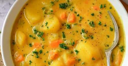 A bowl of classic German Kartoffelsuppe made with potatoes, carrots, leeks, celery, fresh parsley, and sliced sausages, served hot with rustic bread on the side.