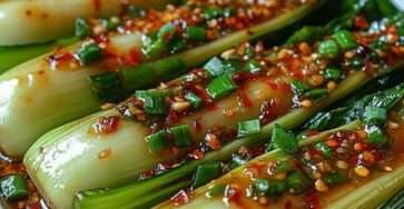 Baby bok choy halves glazed with ginger garlic chili sauce, topped with sliced green onions and sesame seeds in a skillet