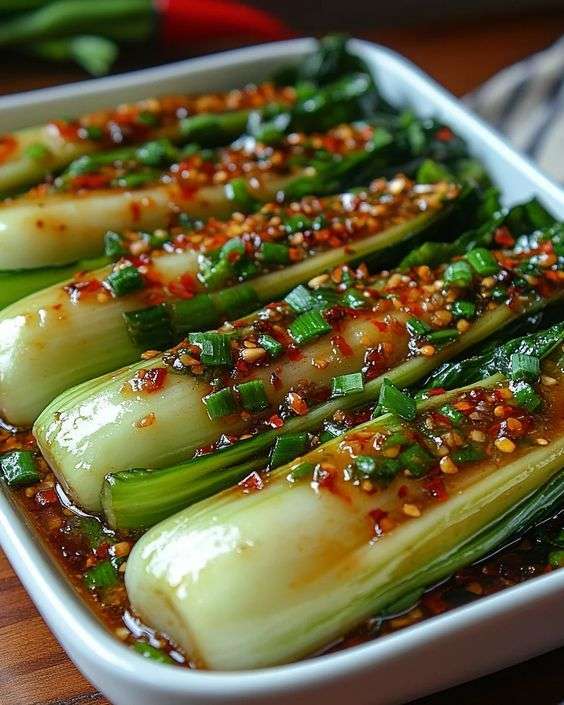 Baby bok choy halves glazed with ginger garlic chili sauce, topped with sliced green onions and sesame seeds in a skillet
