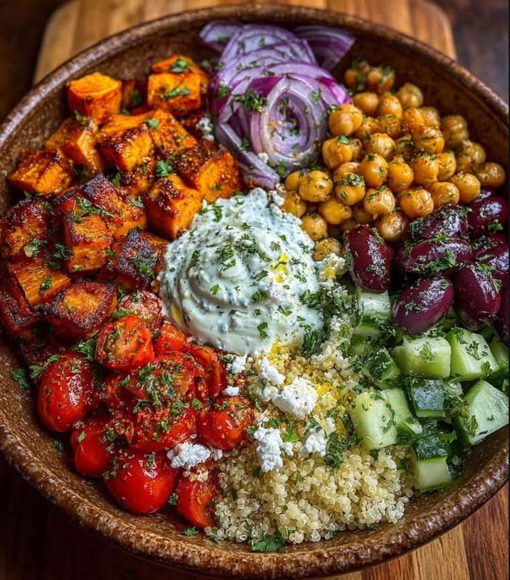 Mediterranean quinoa bowl with roasted sweet potato cubes and crispy chickpeas, cherry tomatoes, cucumbers, red onion, olives, feta, and tzatziki