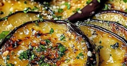 Golden roasted eggplant rounds on a baking sheet topped with minced garlic, lemon zest, and chopped parsley, served as a Mediterranean side dish