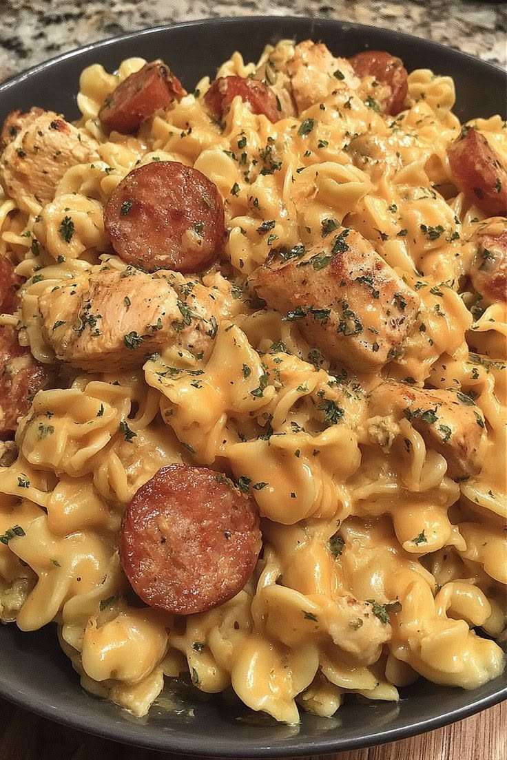 A bowl of crockpot cheddar ranch chicken and sausage pasta with creamy sauce, melted cheese, sliced sausage, and tender chicken pieces garnished with parsley.