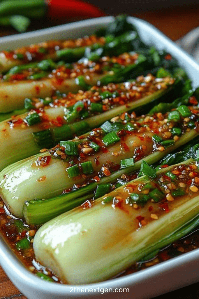 Baby bok choy halves glazed with ginger garlic chili sauce, topped with sliced green onions and sesame seeds in a skillet