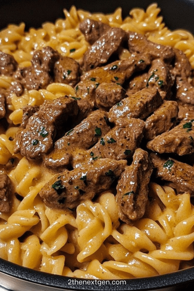 Creamy pasta tossed with seared steak strips in a garlic butter Parmesan cream sauce, finished with parsley and black pepper in a skillet