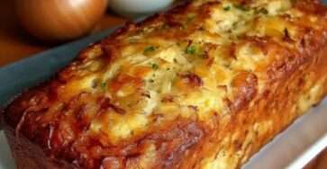 Golden loaf-style savory cake sliced on a board, filled with caramelized onions and melted cheese, with a lightly browned crust and soft moist crumb.