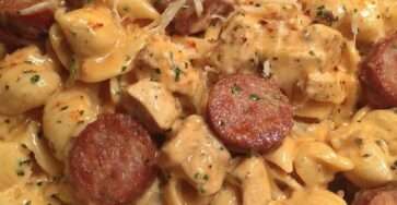 Creamy pasta in a skillet with pieces of chicken and browned smoked sausage slices, coated in a cheesy garlic cream sauce and topped with parsley