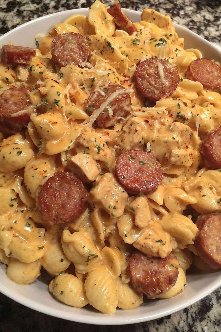 Creamy pasta in a skillet with pieces of chicken and browned smoked sausage slices, coated in a cheesy garlic cream sauce and topped with parsley